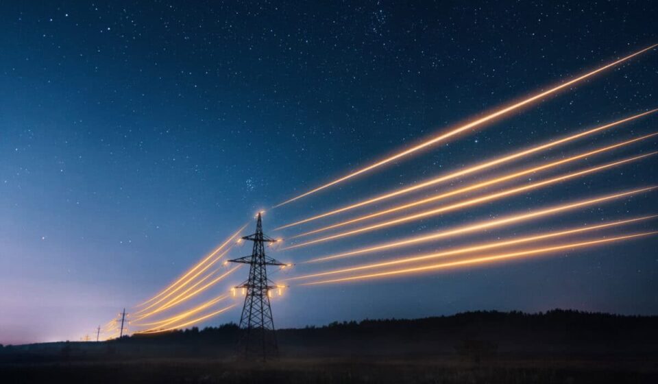 Electricity transmission towers with orange glowing wires against night sky