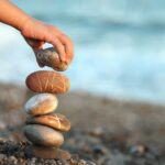 A person builds a rock tower on a beach.