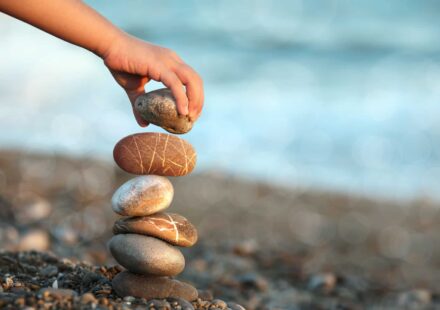 A person builds a rock tower on a beach.