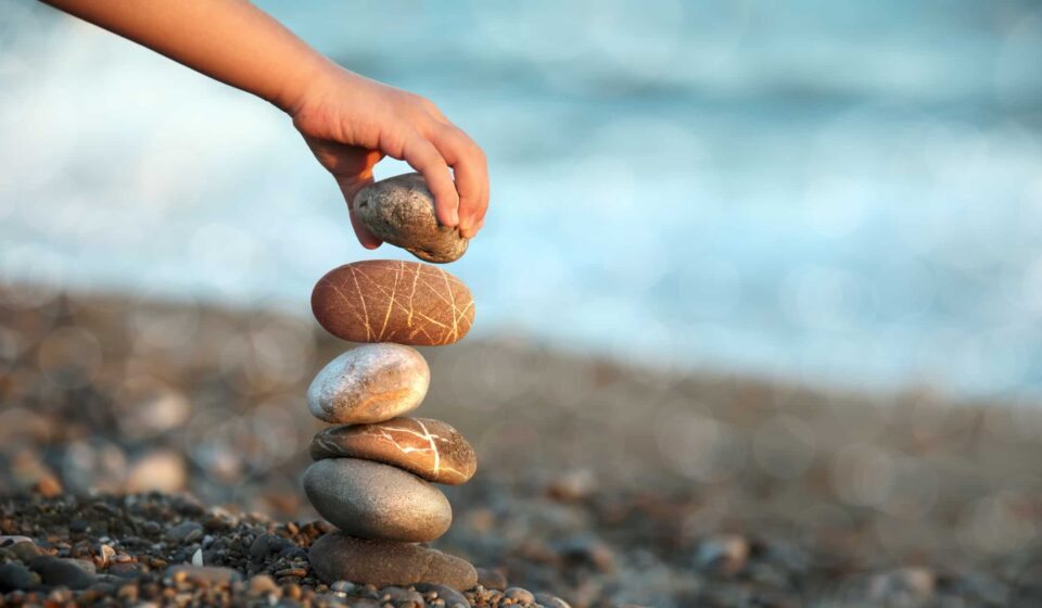 A person builds a rock tower on a beach.