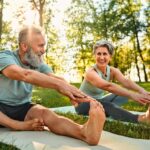 senior man and woman stretch their legs on yoga mats outside