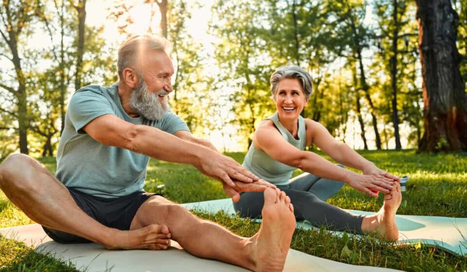 senior man and woman stretch their legs on yoga mats outside