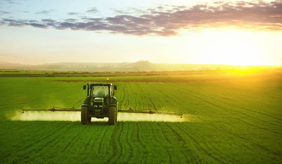 Tractor spraying a field of wheat with fertilizer