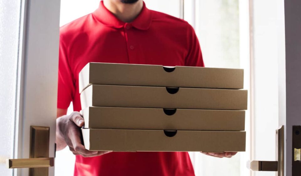 worker carries stack of pizza boxes for delivery